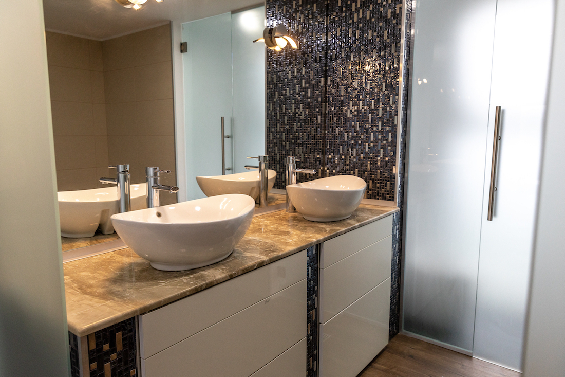 Interior of a bathroom with granite countertop, two sinks, a big mirror and a patterned wall